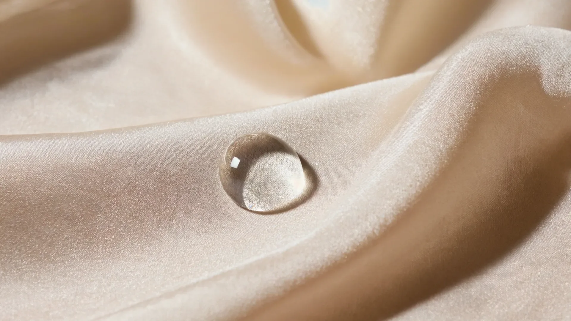 A single droplet of water on pale silk fabric, symbolising deep skin hydration